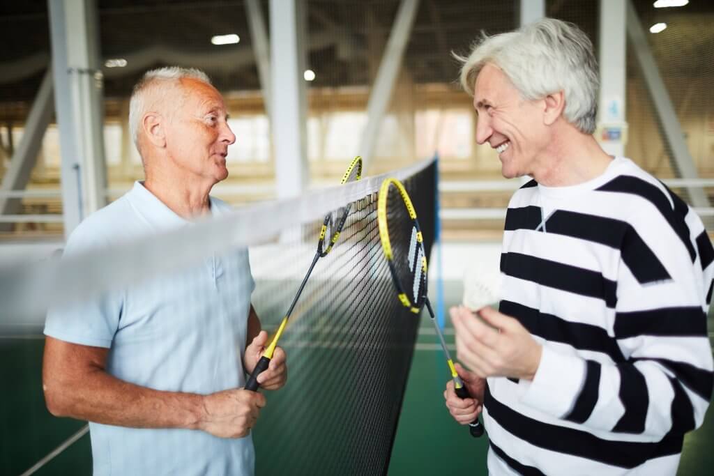 Two elder badminton players, chatting at the net