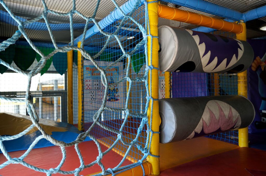 Inside Xcel Leisure Centre Creche play area with roller shark, a roped netting and colourful soft play flooring.