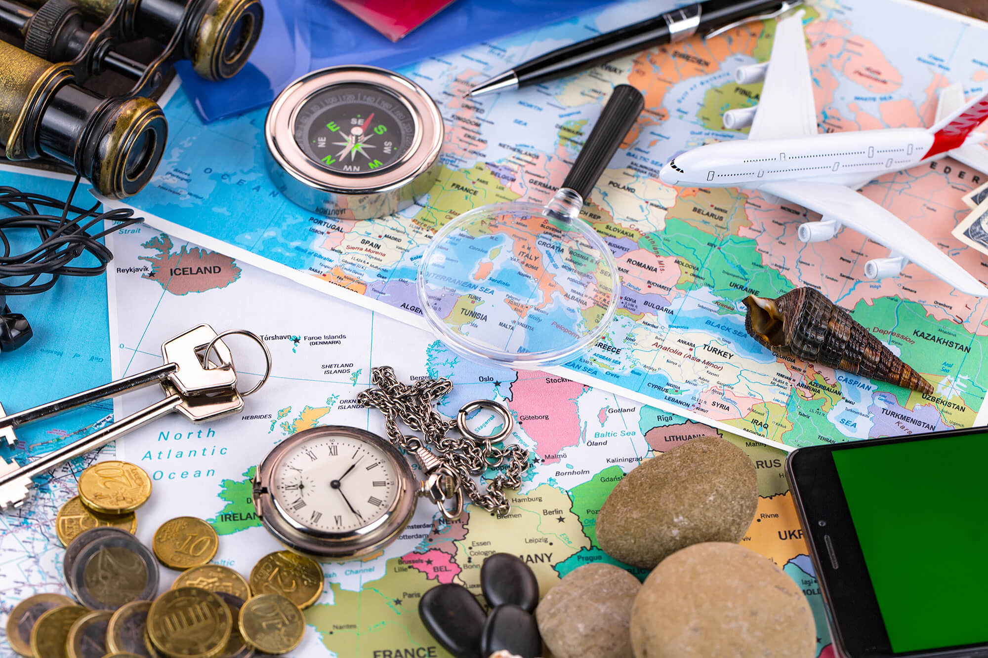 Various explorer and adventure inspired items lay out on the desk. From a toy plane, to compass, to keys and coins.