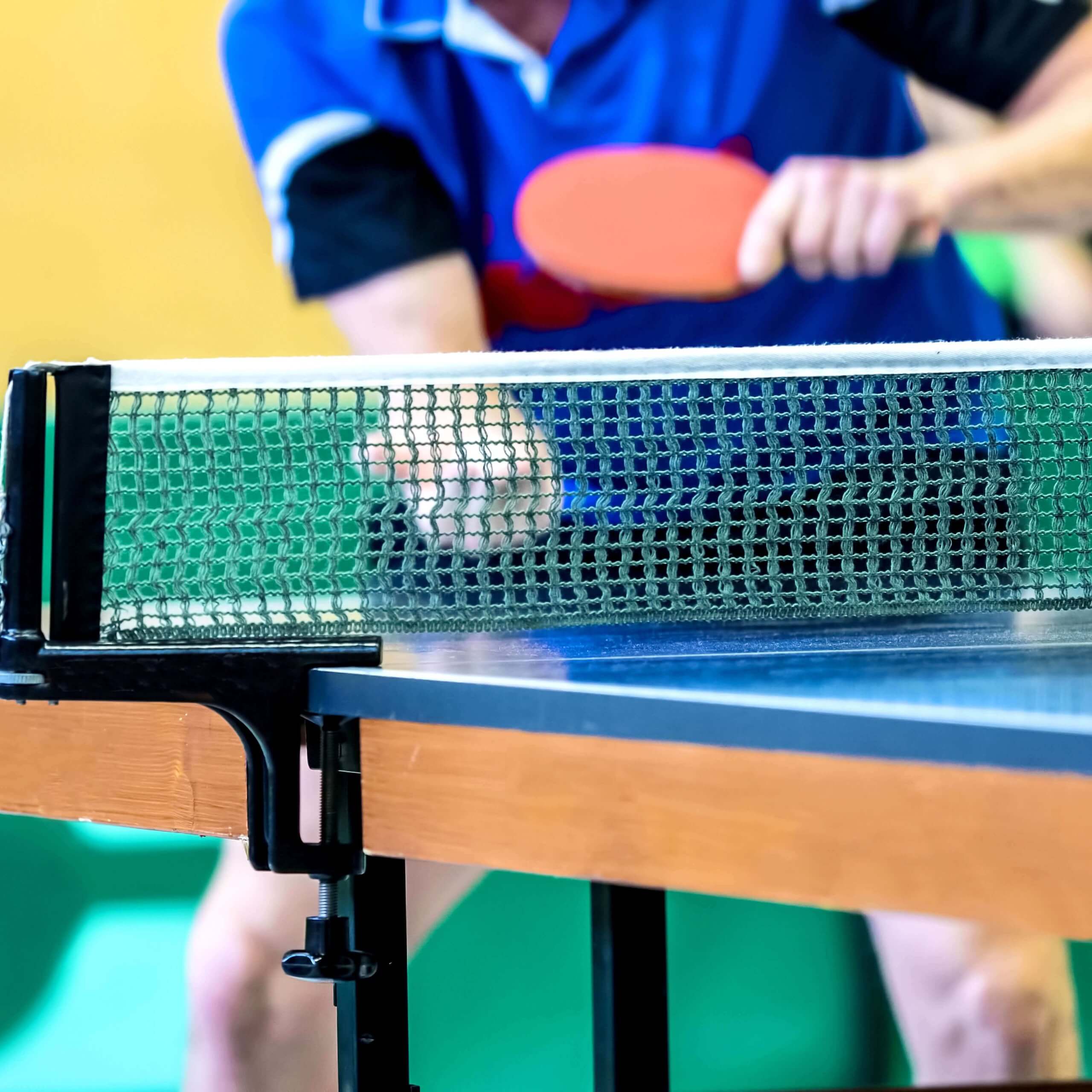 Focused on the net, an out of focused player is in mid shot at a table tennis table.