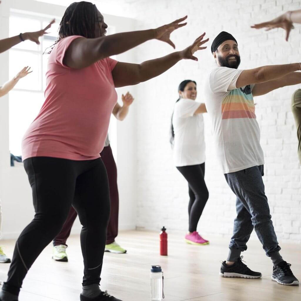 Multi Ethnic group of participants take part in a zumba routine, their arms stretched outwards.